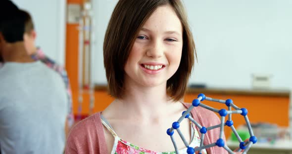 Portrait of happy schoolgirl experimenting molecule model in laboratory alt