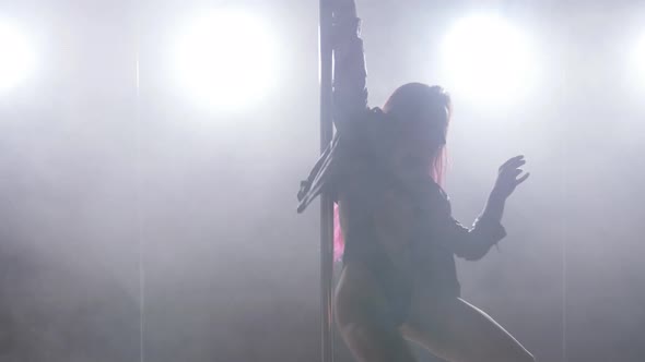 Young Woman on a Pole Dancing in a Dark Room with Backlight and Smoke alt