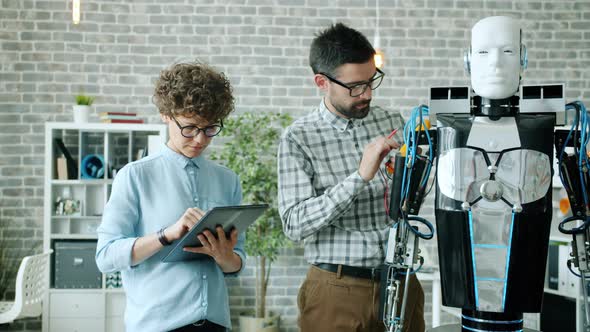 Girl and Guy Testing Robot Functions Using Modern Equipment Tablet in Office alt