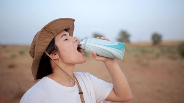 Woman drinking water in desert field alt