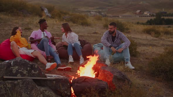 Friendly Tourists are Sitting Around Campfire Drinking Cocktails and Speaking alt