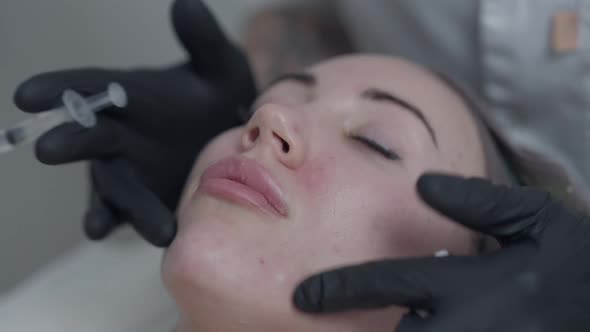 Closeup Beautician Hands in Gloves Massaging Botox Injections on Face of Slim Young Woman alt