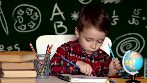 Cute child boy doing homework. Clever kid drawing at desk. Schoolboy. alt