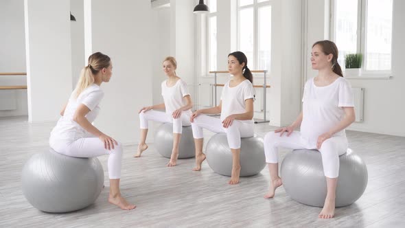 Group of Young Pregnant Women Doing Relaxation Exercise on Fitball with Trainer
