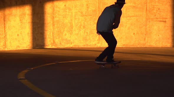 Silhouette of a young man skateboarding in a parking garage at sunset. alt