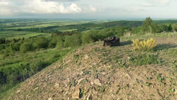 Guy Siting a Song Sitting on the Couch on a High Mountain Where you Can See the Clouds and the alt