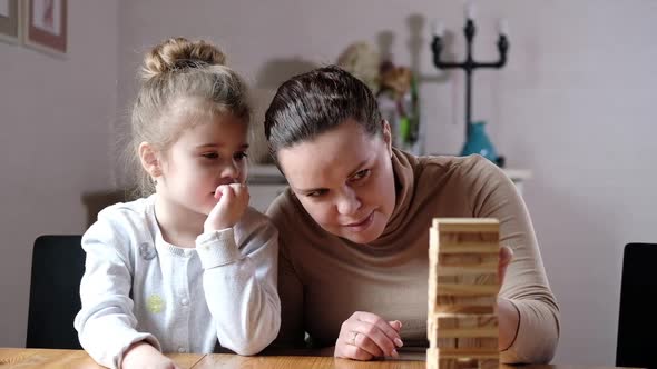 Happy adult parent mom helps cute preschooler daughter play toys together
