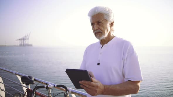 Portrait of Retirement Handsome Senior Man Using Tablet Computer on Seafront Slow Motion alt
