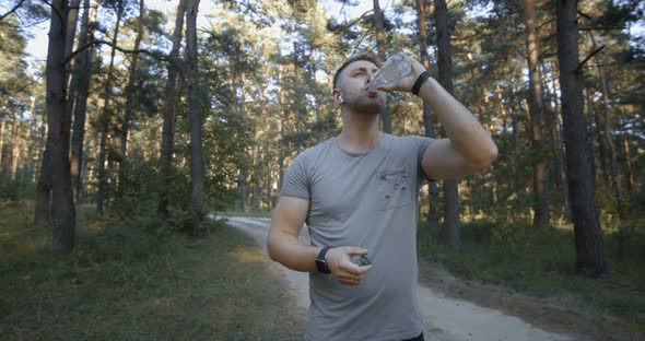 Muscular Man Drinking Water After Workout at Forest alt