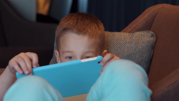 Child Lying in Arm Chair and Watching Cartoons on Pad alt