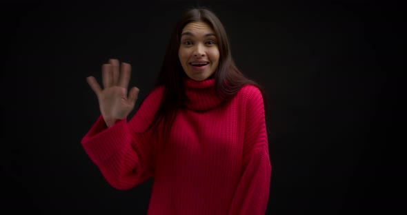 Smiling Asian Woman in a Bright Pink Sweater Waves Her Hand