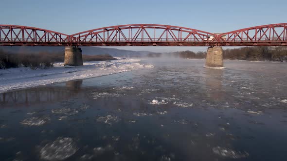 Drone Shot Flies Forward Over the Frozen River and Under the Red Steel Bridge Aerial  Footage alt