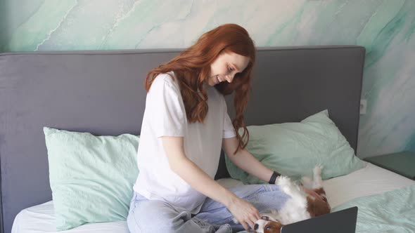 A Pregnant Woman is Sitting on the Bed and Playing with Her Cute Little Dog They are Enjoying a