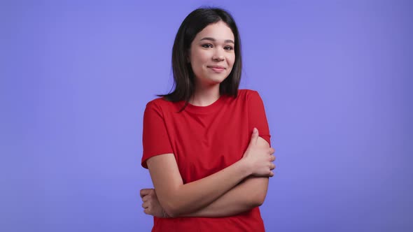 Young Modest and Shy Woman in Orange Tshirt Looking to Camera on Violet Studio Background alt