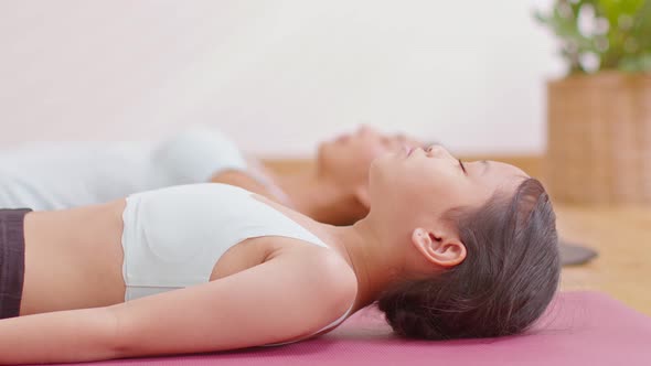 Asian little girl doing yoga dead body pose or nidra meditate with her mom on yoga may at cozy home. alt