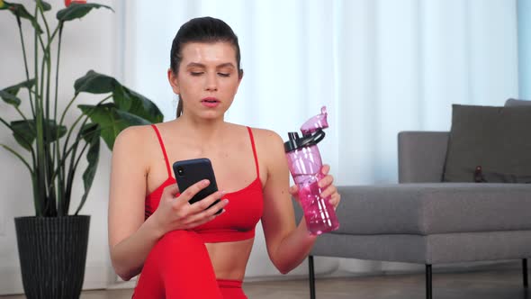 Sportive Woman Drink Water After Active Workout Exercise Uses Smartphone at Home alt