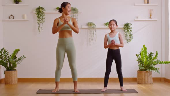Healthy couple mom and little girl doing yoga squat up and down on mat at home.Mother and female dau alt