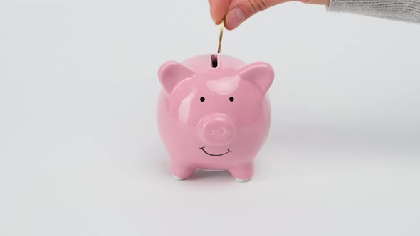 Female hand puts metal coins into the slot of a pink ceramic piggy bank  alt