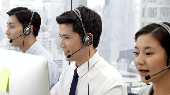 Asian customer services agent wearing microphone headset working with team in call center office