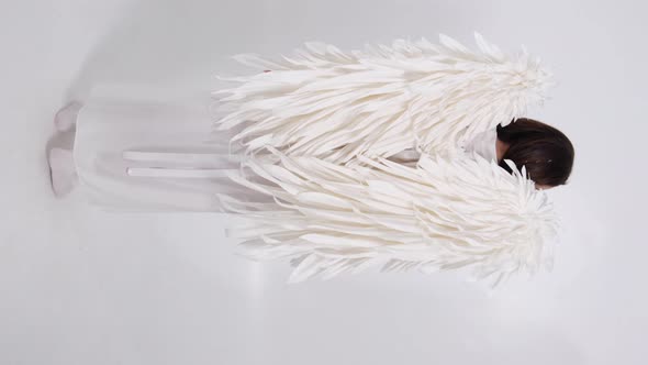 Vertical Video of a Young Girl with White Wings on a White Background alt