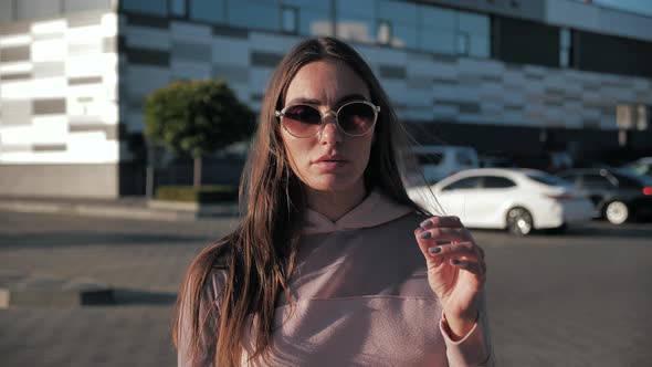 Portrait of Beautiful Young Woman with Glasses Looking Into Camera in Slow Motion As Wind Blows Her alt