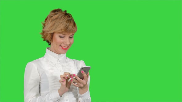 Young Attractive Woman Works on Smartphone and Smiles on a Green Screen, Chroma Key alt