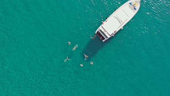 People swimming in sea beside luxury yacht, aerial top down view