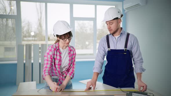 Man and Women in Construction Helmets Make Floor Repairs and Cut Laminate with Tool alt