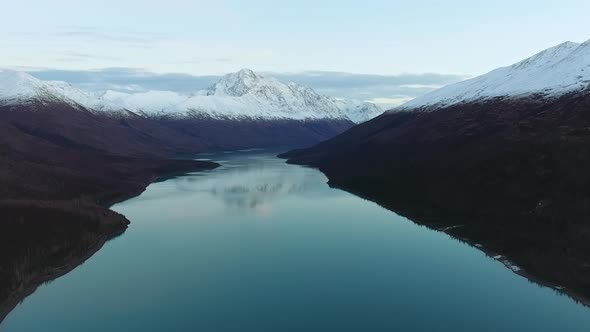 Drone shoots a mirror lake with shores and snow-capped mountains on day in Eklutna Lake, Alaska, USA alt