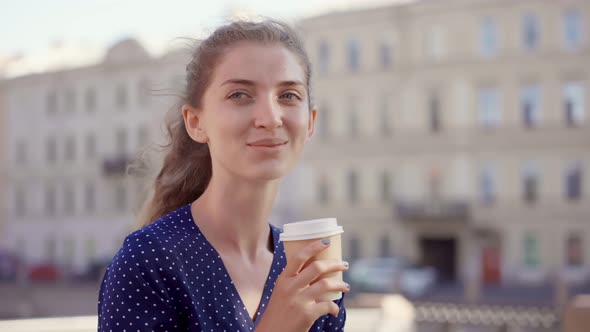 Bokeh Shot of Young Woman Drinking Takeaway Coffee and Looking Away Outdoors alt