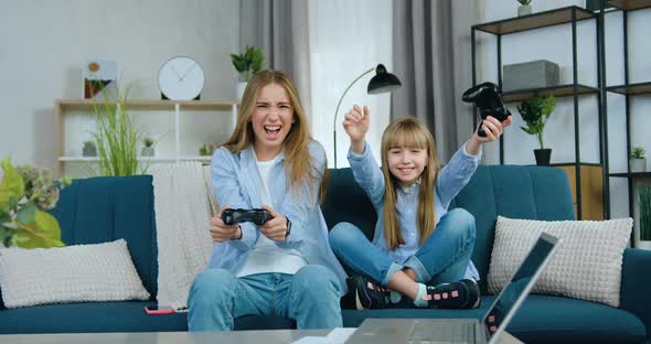Two Different Ages Girls Playing Video Games Using Joysticks and Celebrating Victory alt