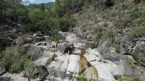 Drone flying over people relaxing on rocks of Cascatas de Fecha de Barjas in Peneda-Geres Park