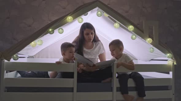 A Mother Reads a Book to Her Sons in a Playhouse