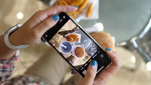 Woman Using Phone To Take Pictures of Burger French Fries and Cola