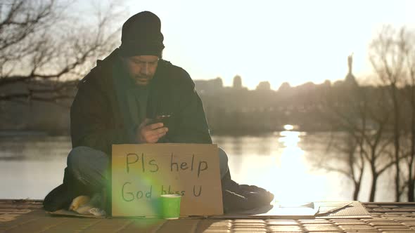 Homeless Man Using Mobile Phone While Begging alt
