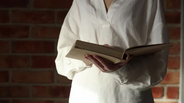Woman in white shirt holding an old book on brick wall background