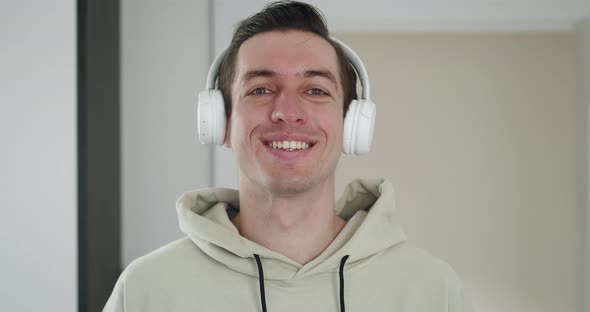 Portrait of a Stylish Man in White Headphones Listening to Music and Looking at the Camera Indoors alt