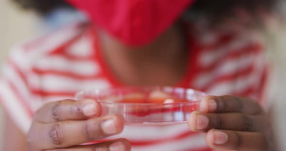 Girl wearing face mask and protective glasses holding container with chemical at laboratory alt
