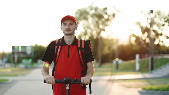 Young Student Works in a Delivery Service With a Red Backpack Rides an Electric Scooter