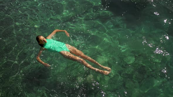 Slow Motion Top View of Sexy Stunning Woman with Nise Buttocks in Green Swimsuit Floating in Clear alt