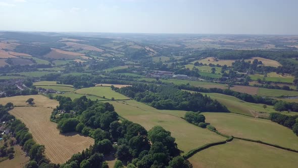 Flying over lush green farm fields in Exeter, UK on summer day, AERIAL PULL BACK alt