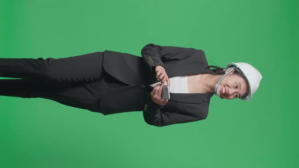 Smiling Asian Female Engineer Using Smartphone And Looking Around While Walking On Green Screen alt