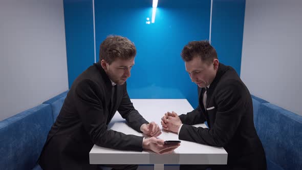 Confident Businessman Showing Online Presentation on Smartphone to Partner Talking and Smiling alt