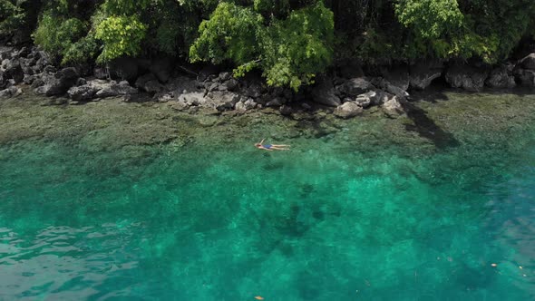 Aerial: woman snorkeling on Pulau Gunung Api coastline coral reef tropical alt