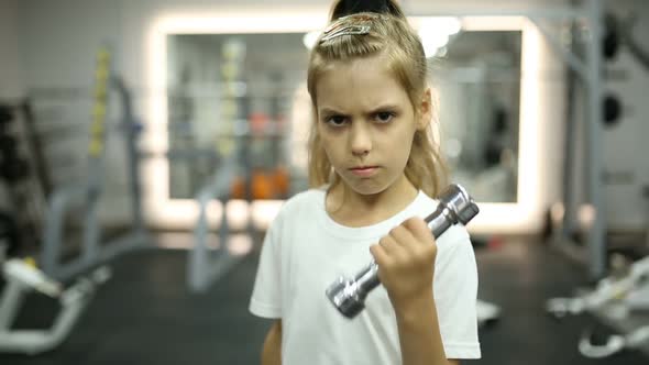 A little girl is lifting dumbbells in a gym