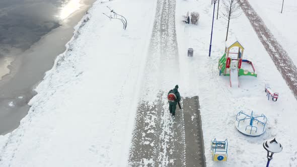 Worker removes snow from pedestrian sidewalk in the park with a blower.