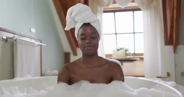 Happy african american attractive woman relaxing in foam bath in bathroom alt