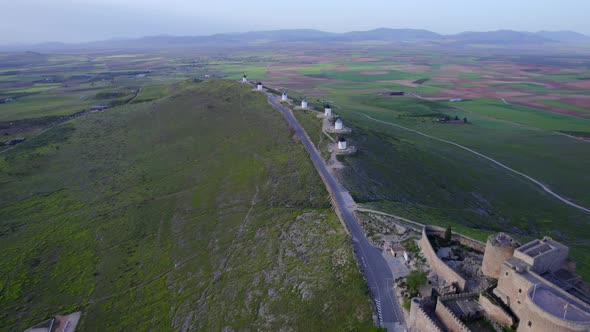 Old white windmills in line on top of a green hill in a traditional Spanish village. Aerial view alt