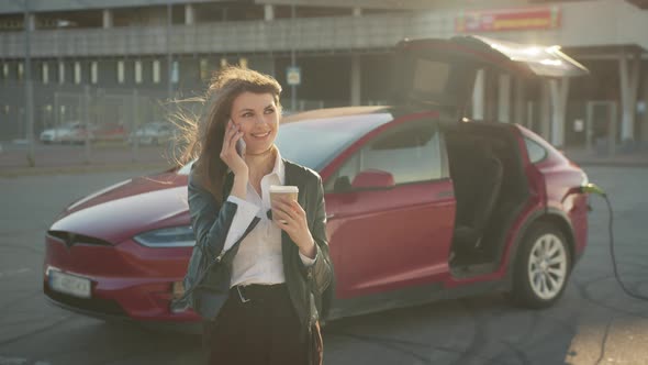 Woman Having Call on Smartphone While Charging Car alt