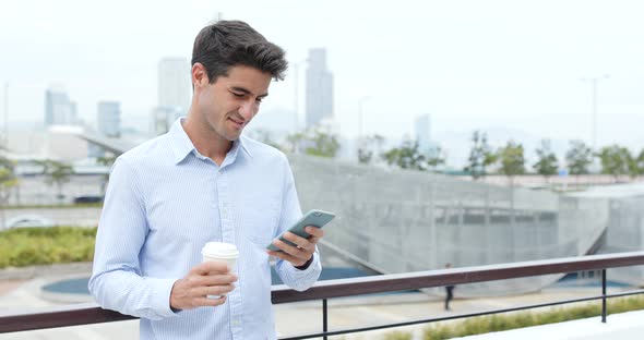 Businessman using mobile phone and holding cup of coffee alt